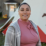 Paulete Poitras, souriante, devant un tipi blanc décoré d'un motif rouge et de l'image d'un cheval.