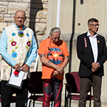 Des personnes debout sur une estrade à la Colline du Parlement lors de la cérémonie de lever du drapeau des survivants en 2025.