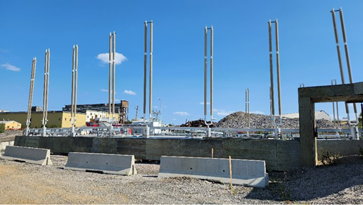 A series of tall metal poles protrude from a concrete block on an industrial site