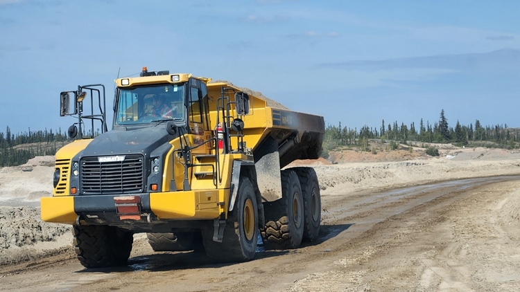 An articulated rock drives on a dirt road through a construction site.