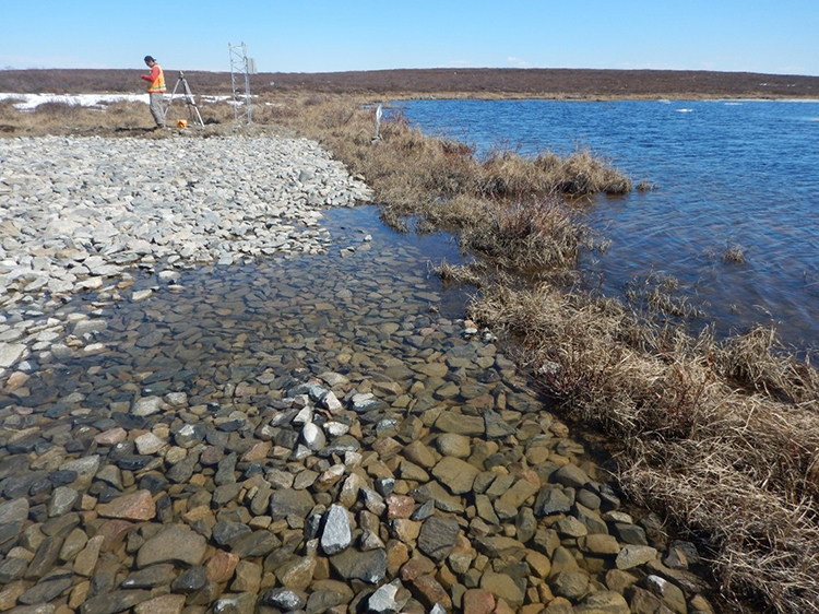 Un travailleur portant un gilet de sécurité se tient sur la rive du lac Hambone avec l'équipement utilisé pour mesurer les niveaux d'eau.