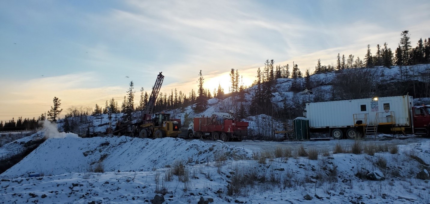 Équipement de forage et machinerie à l'œuvre sur le chantier pour les travaux de stabilisation du sous-sol. Le terrain est recouvert de neige et le soleil éclaire les arbres en contrejour.